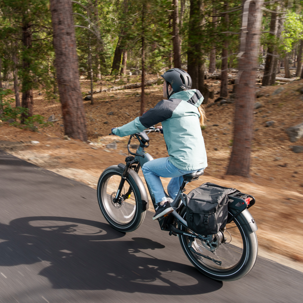 Rear view of a rider taking the Nomad Pro through a wooded path with fat tires on packed dirt.