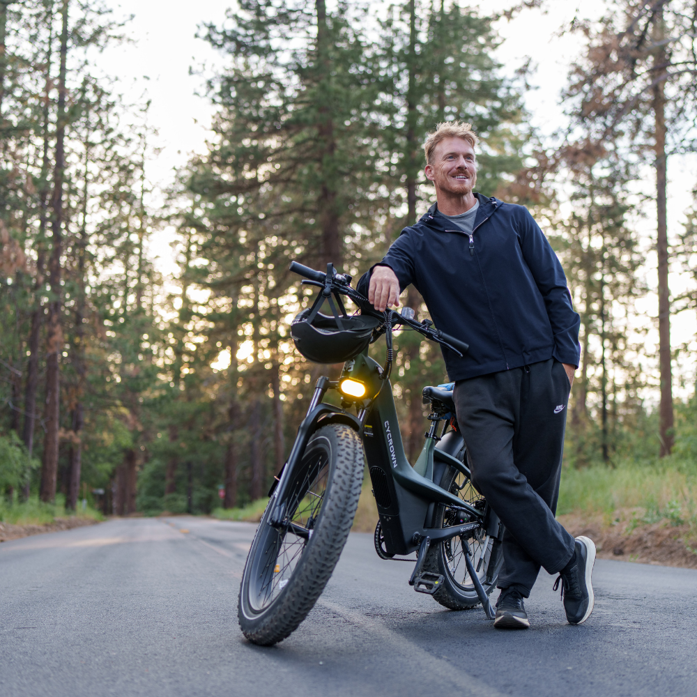 Rider standing beside a headlight-lit Nomad Pro in a forest at dusk.