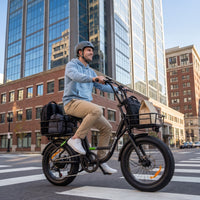 Helmeted commuter riding the isinwheel U7 across a downtown crosswalk with a messenger bag on the rear rack and office buildings in the background