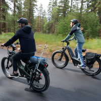 Two Nomad Pro riders traveling along a wooded road with rear racks and fat tires visible.