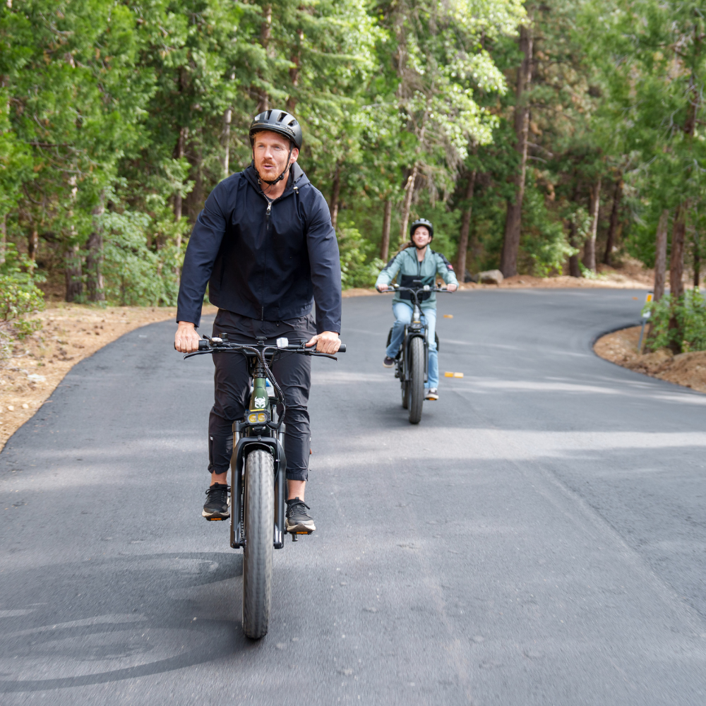 Front view of two Nomad Pro riders approaching on a forest road with headlights and fat tires visible.