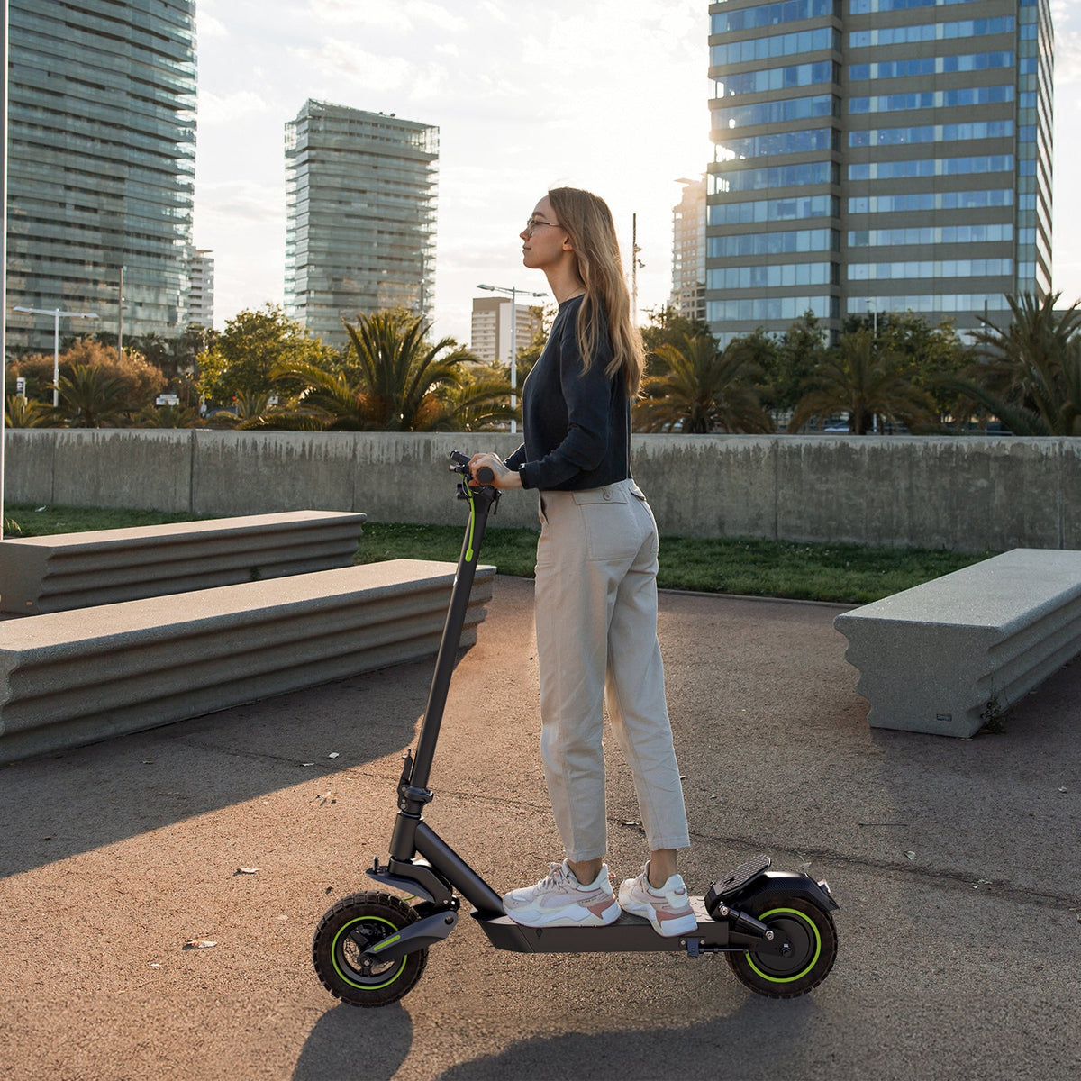 Woman standing on an S10Max commuter scooter near benches and modern city buildings
