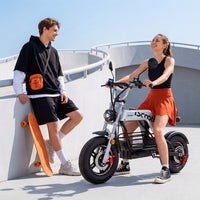 Two riders standing beside the parked iScooter DX5Pro on a sunny urban walkway, showing its moped-style size and seat height.