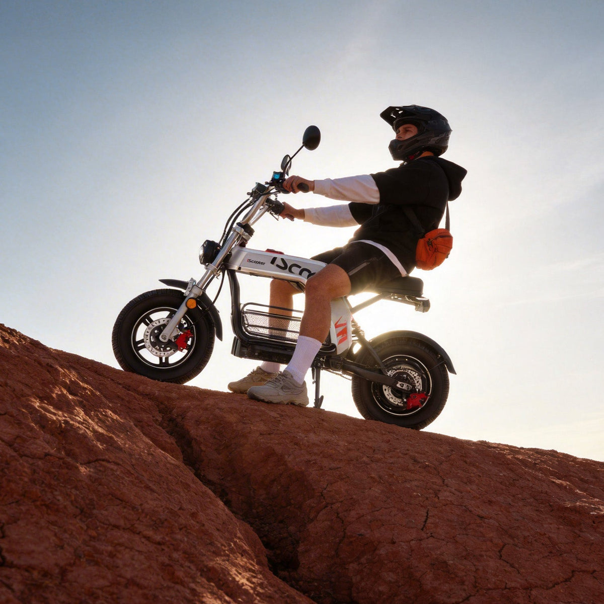 Side silhouette of a rider climbing reddish dirt on the iScooter DX5Pro, useful for judging the scooter's seated off-road posture.