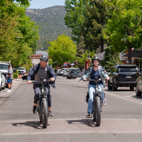 Two helmeted riders approaching on Cycrown Nomad Pro e-bikes across a paved outdoor path.