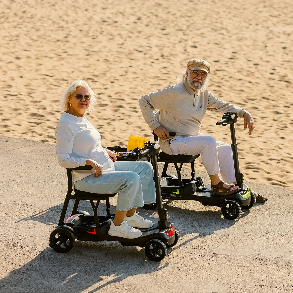 Two ScootNGo Lite mobility scooters parked by adults near a sandy waterfront