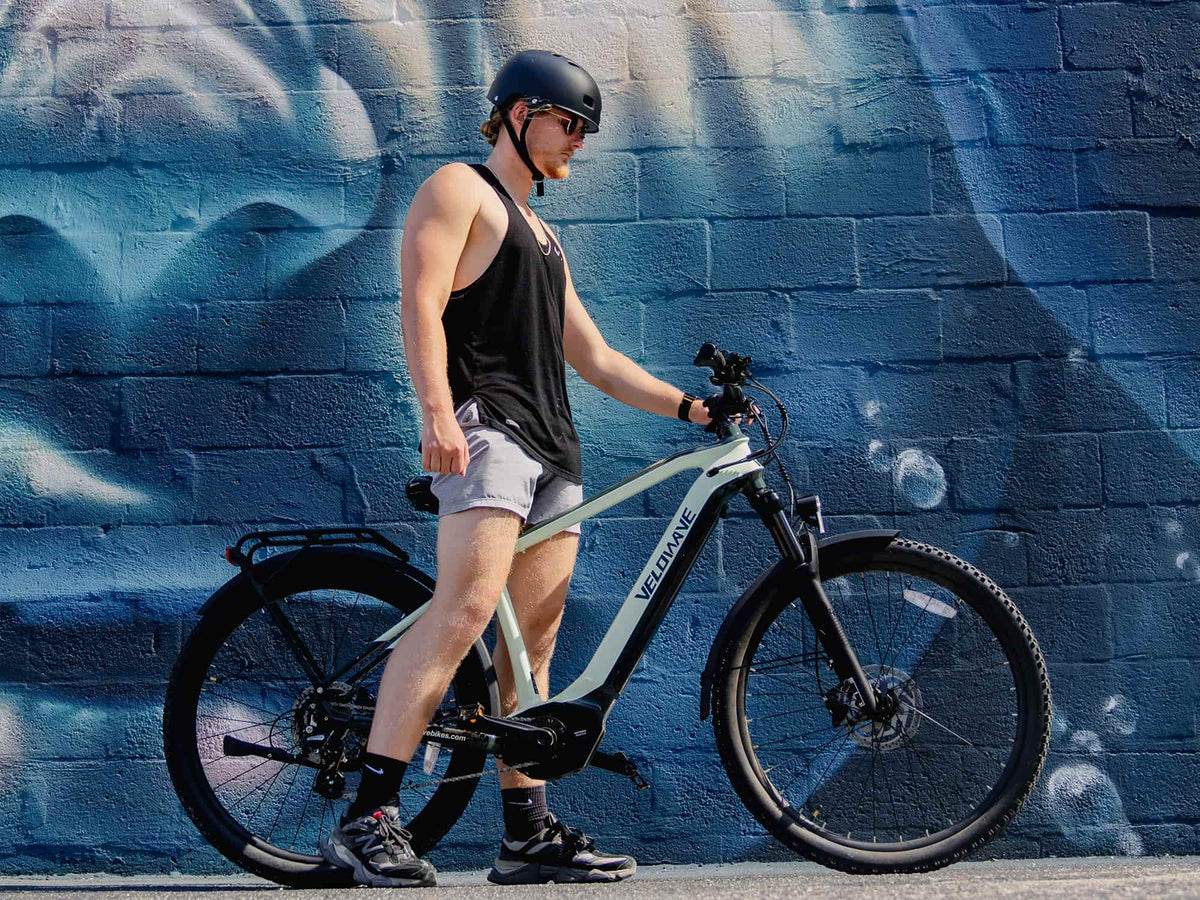 Helmeted rider walking a Macaron Green Swift M beside a blue mural
