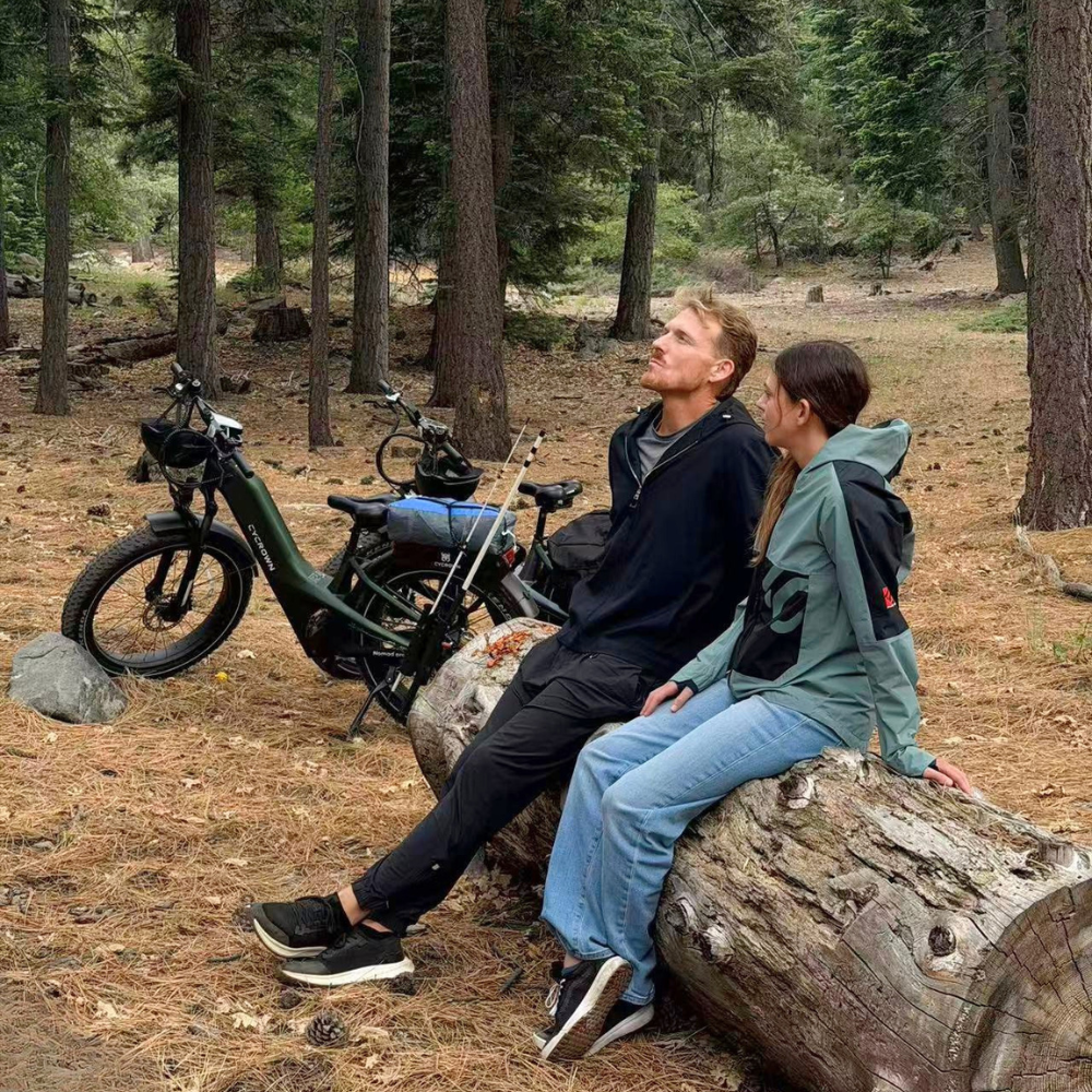 Two riders resting beside their Nomad Pro e-bikes on a wooded trail stop.