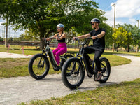 Two riders on Velowave step-through electric bikes on a paved park path