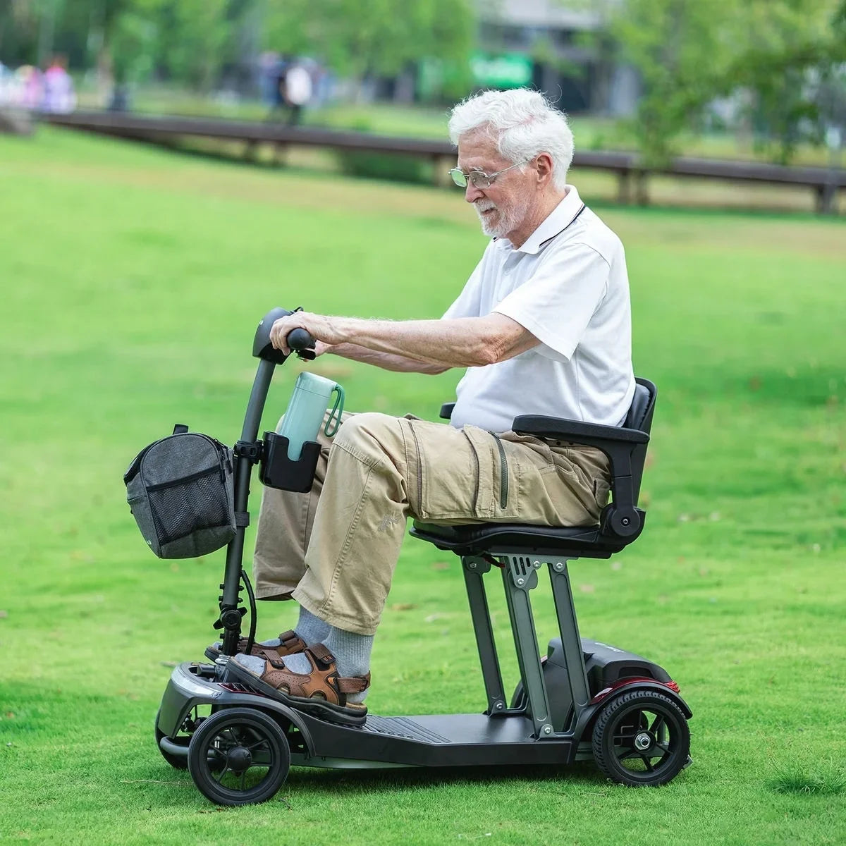 Adult riding a ScootNGo Folo mobility scooter on grass with a front bag