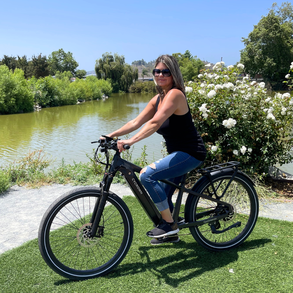 Woman riding the black Dremax beside a lake on a paved recreational path.