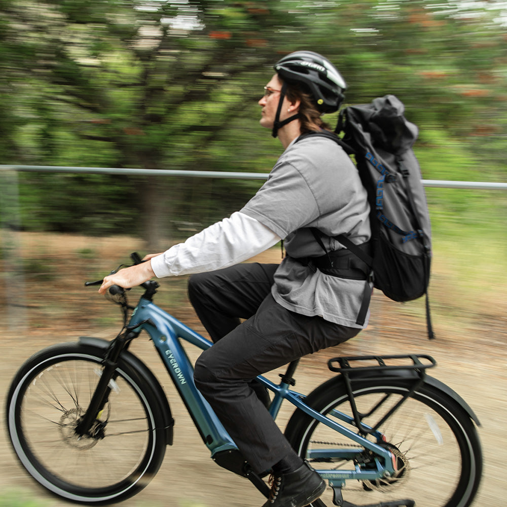 Backpack-wearing rider cruising on the teal Dremax, showing the bike as a daily commute option.