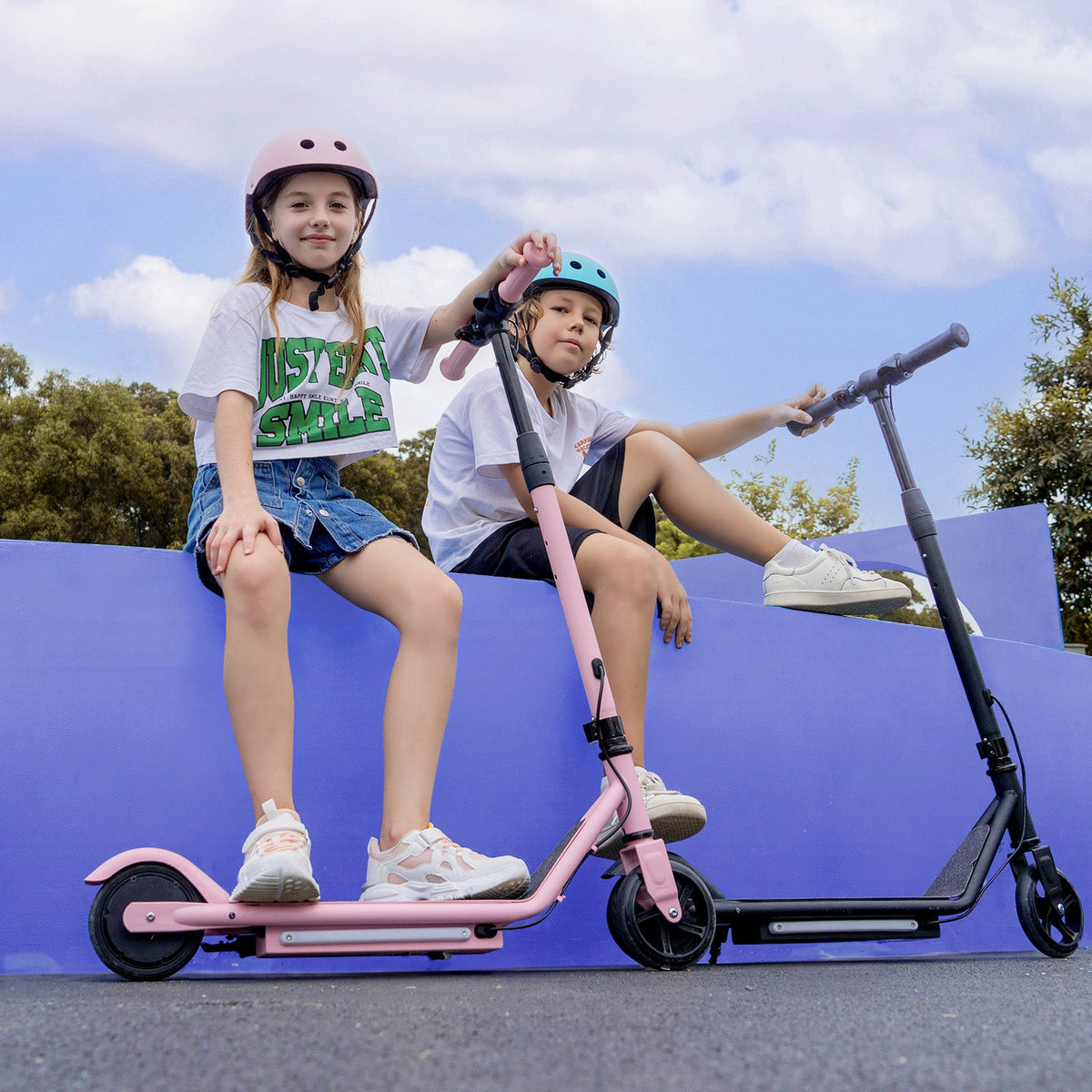 Two helmeted children sitting with pink and black isinwheel S2 scooters
