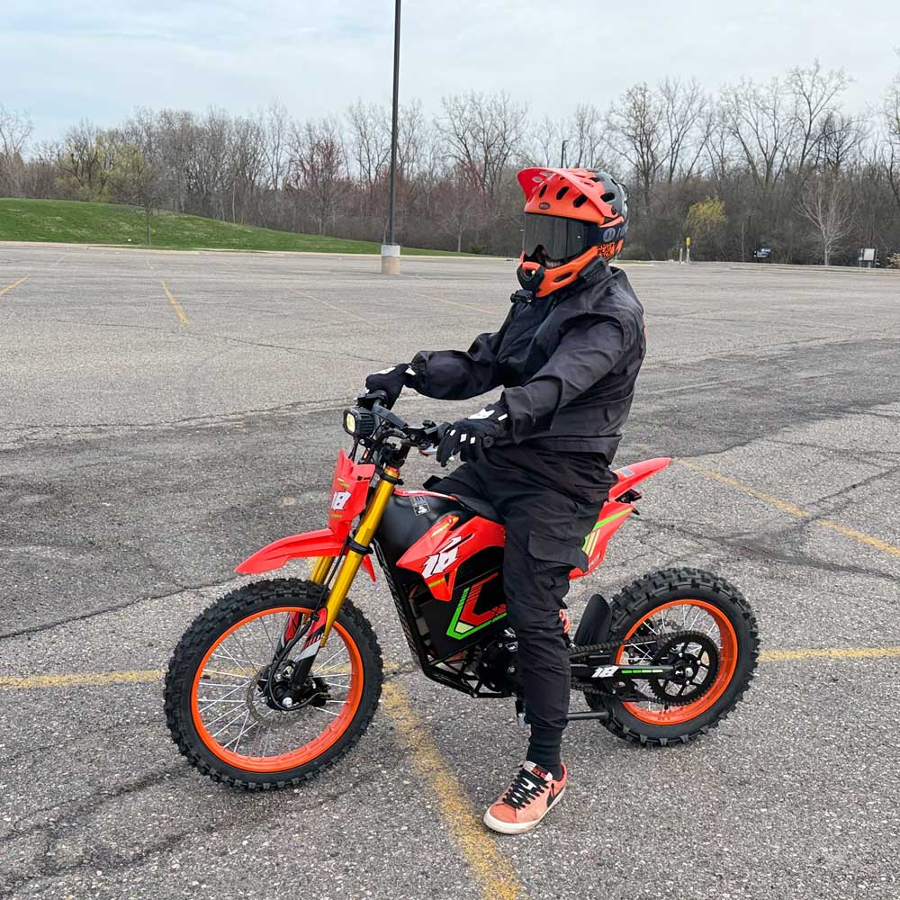 HappyRun F18 motocross-shaped electric dirt bike with a 6000W peak mid-drive motor, 245 Nm of peak torque through a chain drive, knobby off-road tires, full suspension, hydraulic disc brakes with a 190mm rotor, IPX5 water resistance, and a motocross frame in red and black with number plates