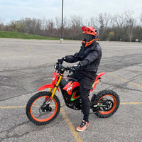 HappyRun F18 motocross-shaped electric dirt bike with a 6000W peak mid-drive motor, 245 Nm of peak torque through a chain drive, knobby off-road tires, full suspension, hydraulic disc brakes with a 190mm rotor, IPX5 water resistance, and a motocross frame in red and black with number plates