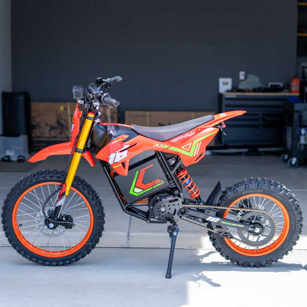 HappyRun F18 motocross-shaped electric dirt bike with a 6000W peak mid-drive motor, 245 Nm of peak torque through a chain drive, knobby off-road tires, full suspension, hydraulic disc brakes with a 190mm rotor, IPX5 water resistance, and a motocross frame in red and black with number plates