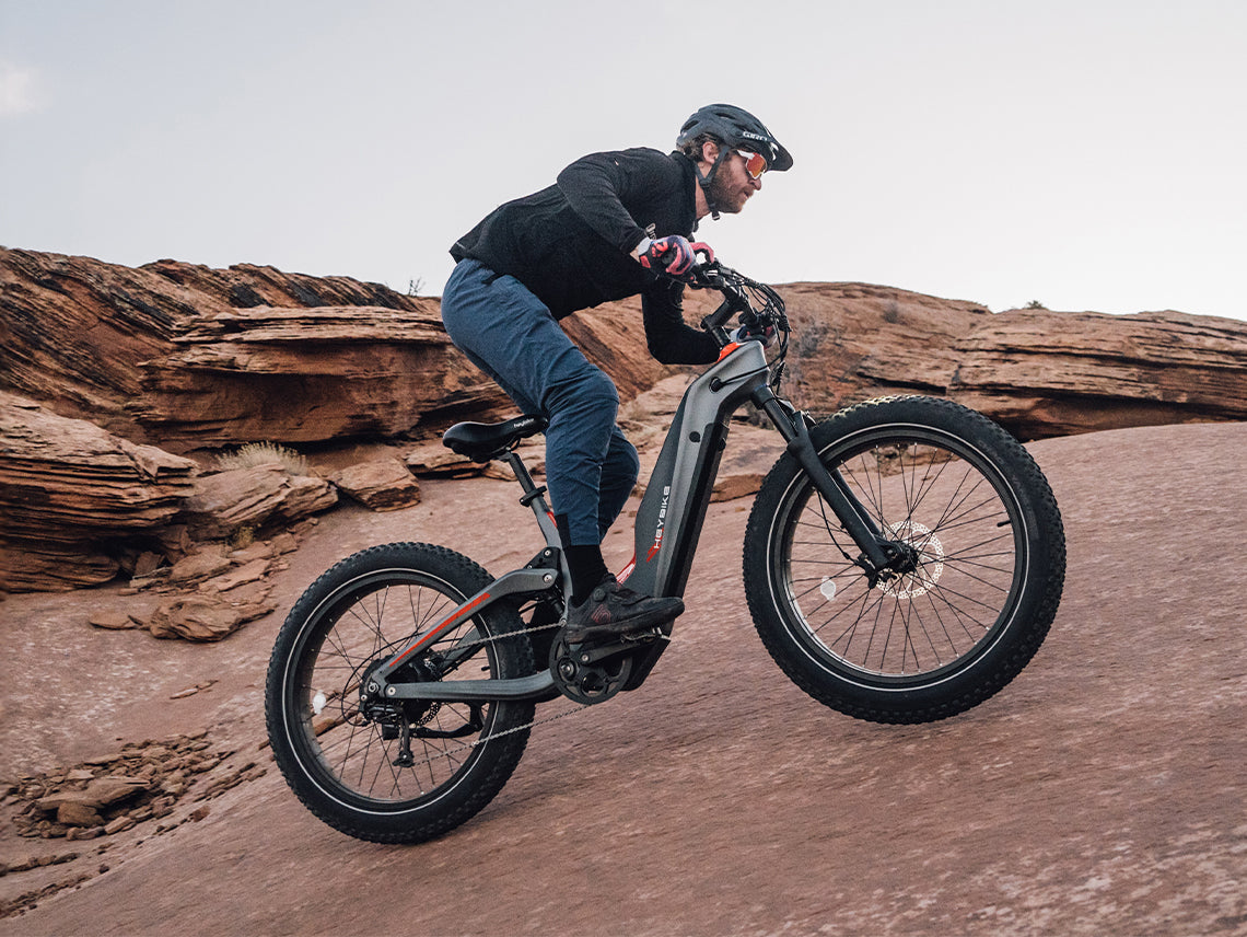 Heybike Hero carbon-fiber full-suspension fat-tire electric mountain bike with two motor configurations (1000W rear hub or 750W mid-drive with torque sensor), step-thru or step-over frame geometry, Shimano 9-speed gearing, hydraulic disc brakes, and UL 2849 certified electrical system