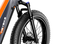 Detail view of the Heybike Hero front fork suspension stanchions, the front hydraulic disc brake caliper and rotor, and the front fat tire knobby tread