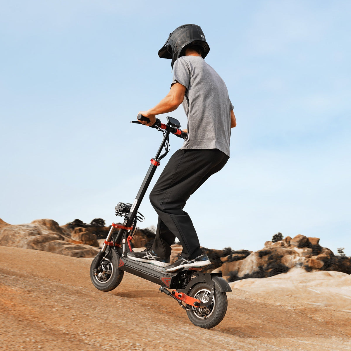 Helmeted rider in a full-face motorcycle helmet riding the iScooter iX8 across a sunlit desert and badlands landscape, showing real-world off-road use